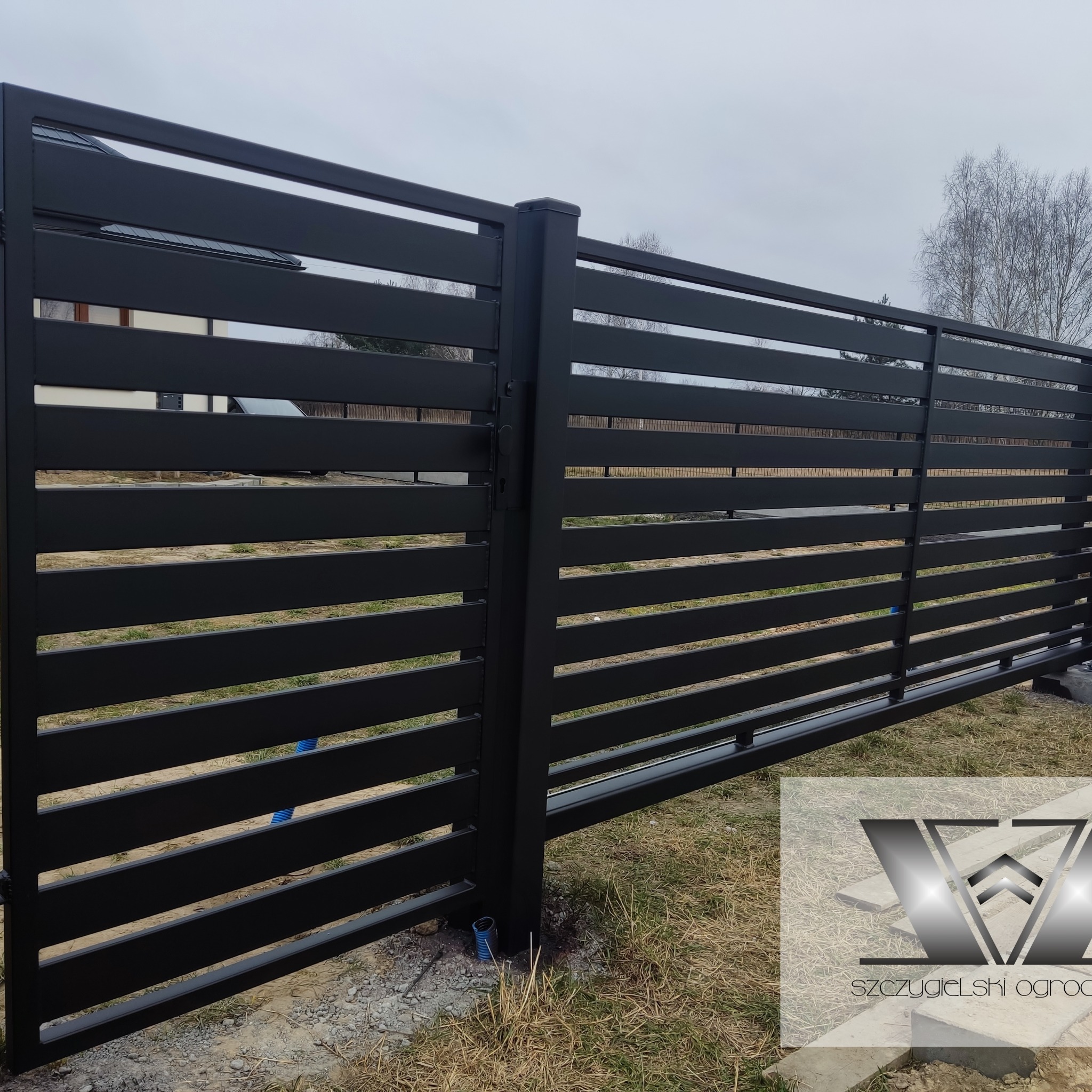 Nowoczesna, czarna brama przesuwna z poziomych profili, zrealizowana w Parczewie, z widocznym logo firmy w prawym dolnym rogu.