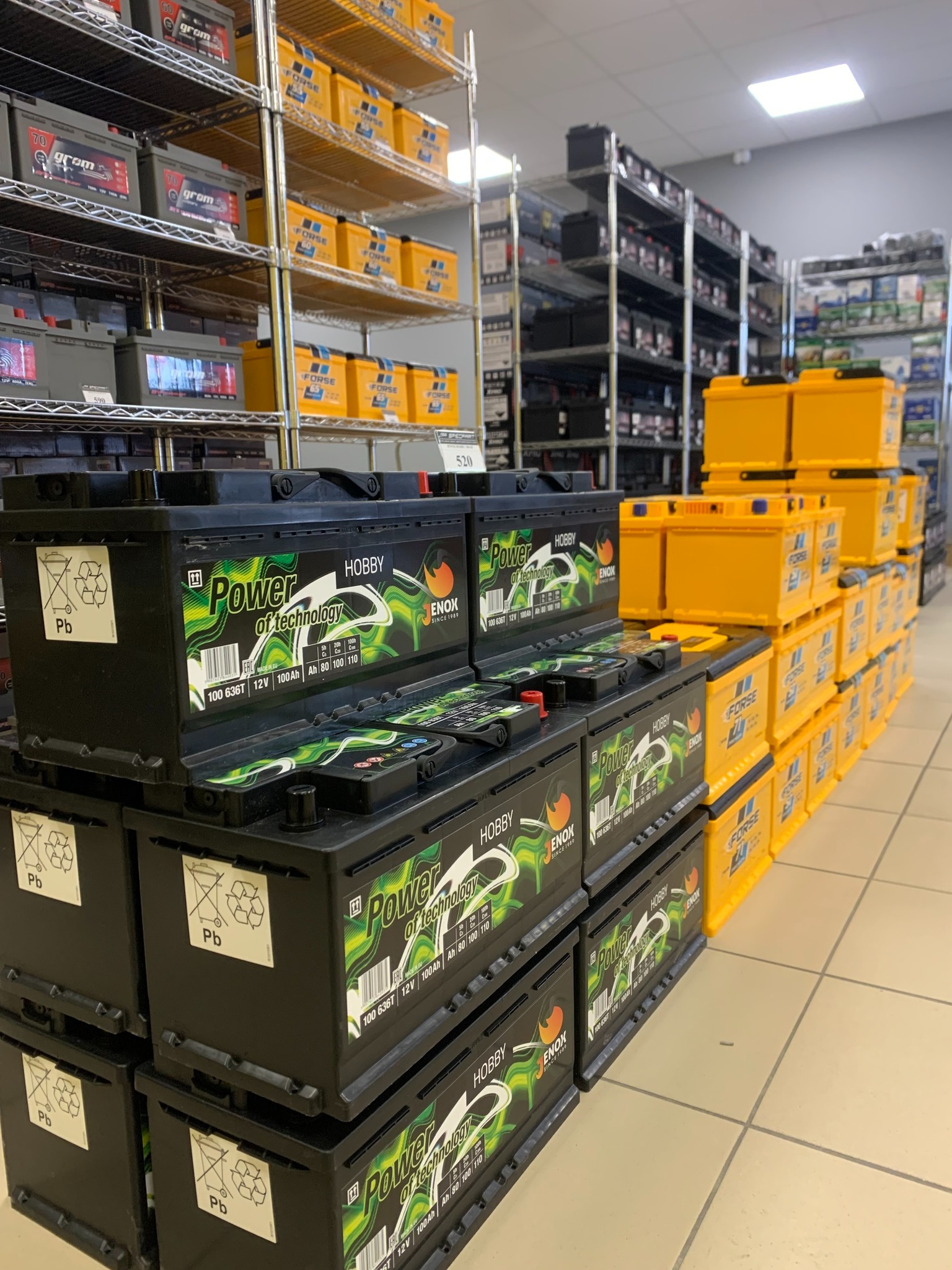 Sklep z akumulatorami samochodowymi: rzędy czarnych akumulatorów marki Enox Hobby i żółtych akumulatorów Forse na metalowych regałach.