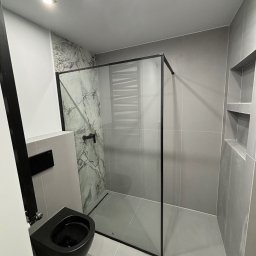 ROJO Radosław Otfinowski - Nowoczesna łazienka w odcieniach szarości z czarną armaturą, kabiną prysznicową typu walk-in z marmurową ścianą i podtynkową toaletą.