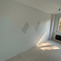 ROJO Radosław Otfinowski - Pokój po malowaniu z motywem gór na ścianie, widoczne promienie słoneczne wpadające przez okno i surowa podłoga.