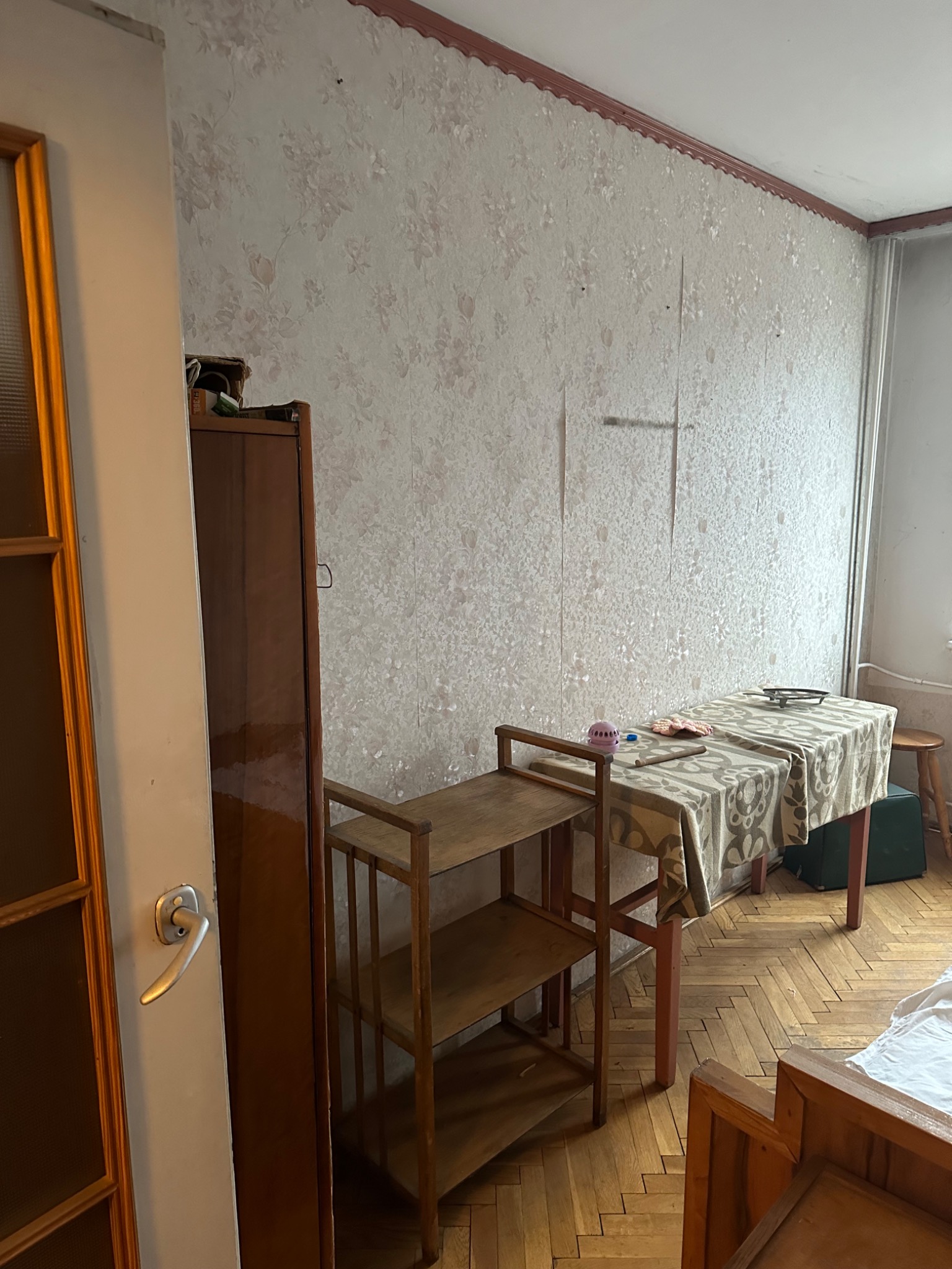 Pokój przed remontem: ściany z odchodzącą tapetą w kwiatowy wzór, drewniana podłoga w jodełkę, meble w stylu retro.
