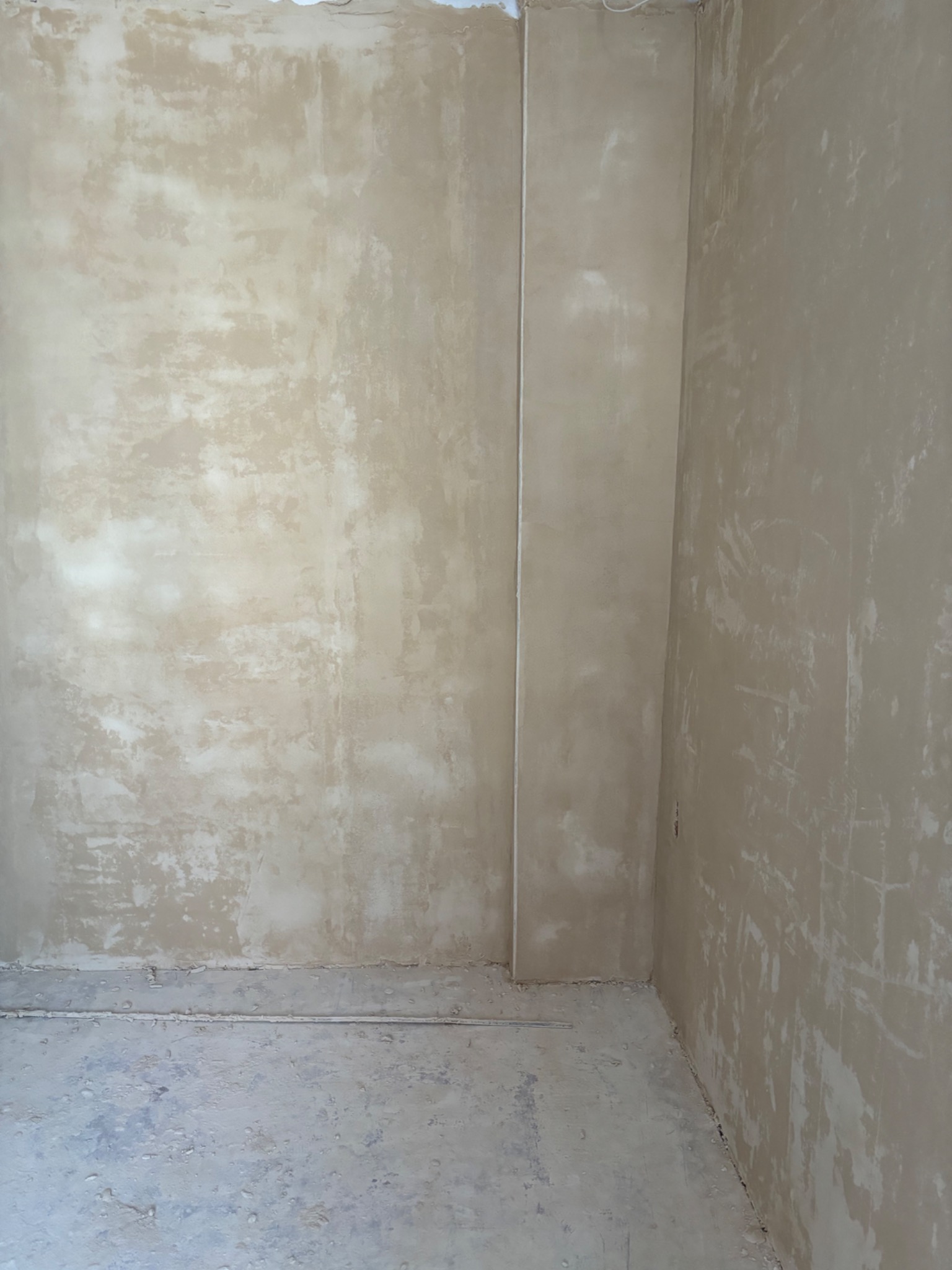 Surowe ściany w rogu pokoju po nałożeniu pierwszej warstwy tynku, widoczne niedoskonałości i nierówności powierzchni.