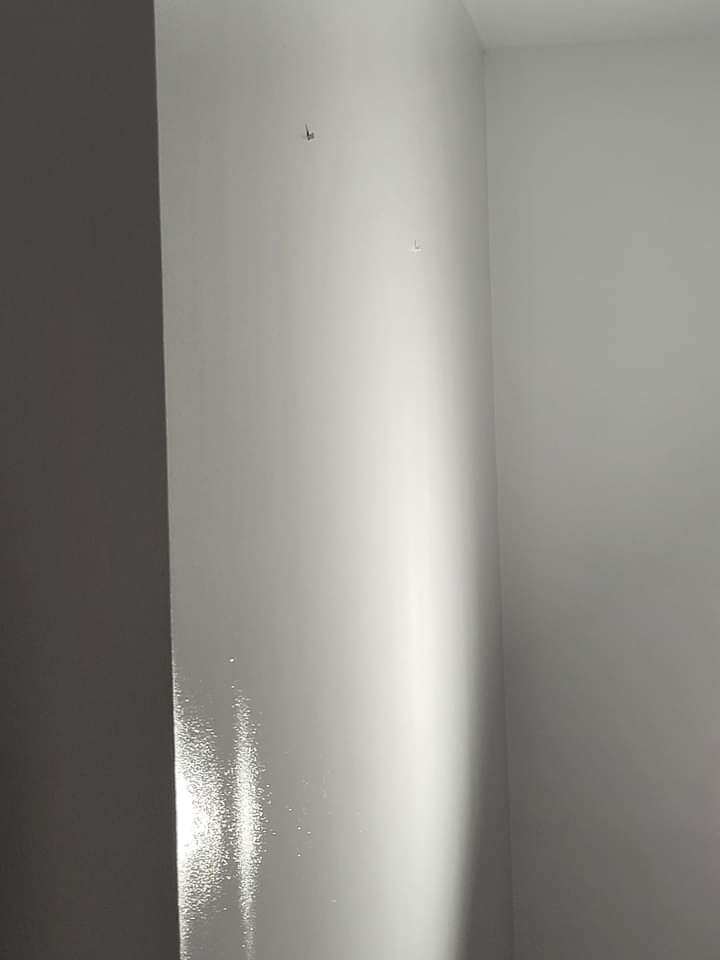 Świeżo pomalowana, biała ściana z widocznymi śladami po niedoskonałościach szpachlowania pod światło, widoczne dwa małe otwory po gwoździach.