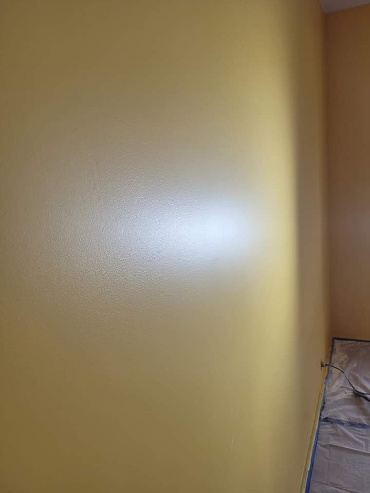 Świeżo pomalowana na żółto ściana w rogu pomieszczenia, widoczne zabezpieczenia folią malarską na podłodze.