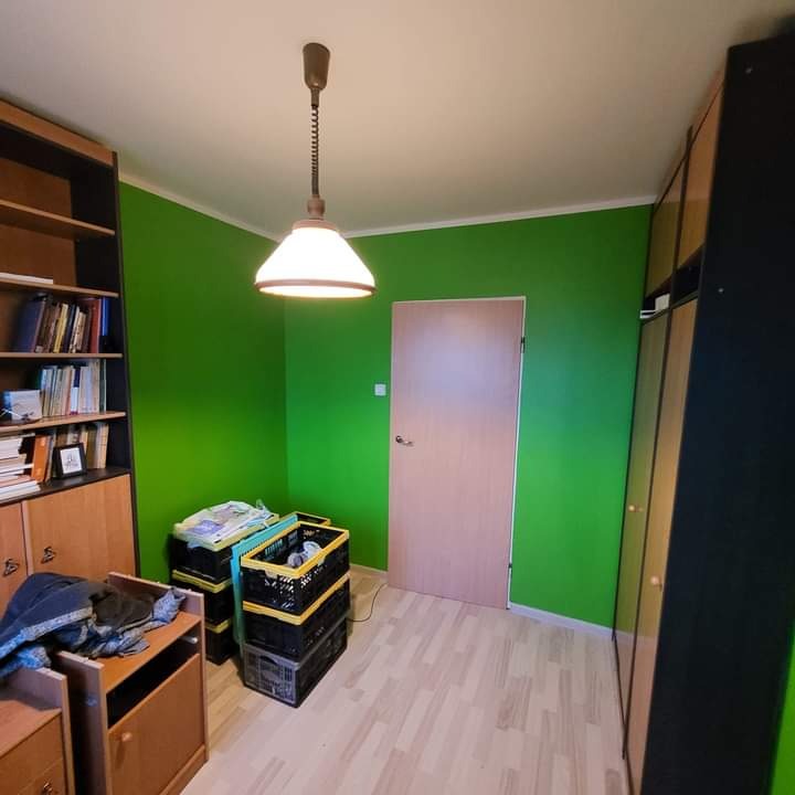 Pomieszczenie po malowaniu ścian na jaskrawy zielony kolor, widoczne meble, skrzynki i lampa wisząca.