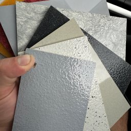 DecorativeGroup - Paleta próbek różnych wykończeń podłóg i ścian prezentowana w Otwocku: od szarych, gładkich po czarne, z brokatem i imitujące marmur.