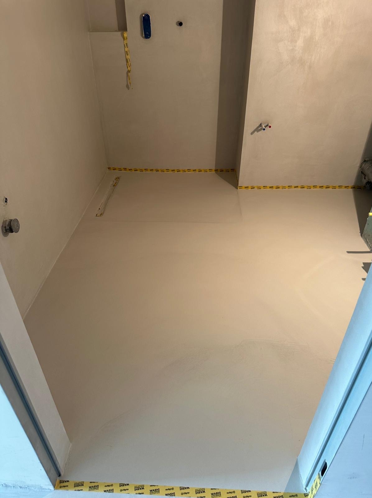 Jasnoszara, gładka powierzchnia w pomieszczeniu z taśmą maskującą na ścianach, widoczne elementy instalacji na suficie, ujęcie z dołu.