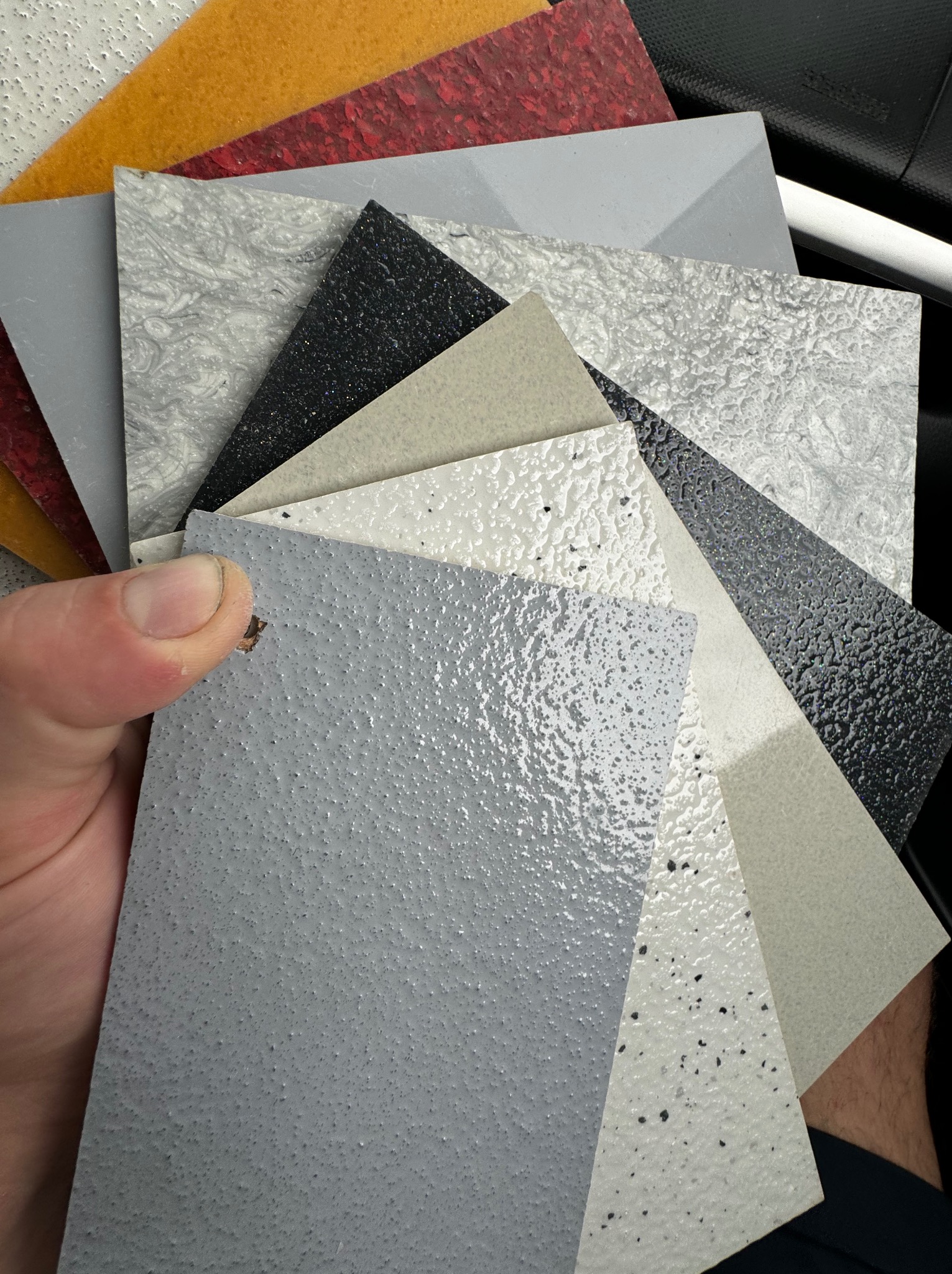 Paleta próbek różnych wykończeń podłóg i ścian prezentowana w Otwocku: od szarych, gładkich po czarne, z brokatem i imitujące marmur.