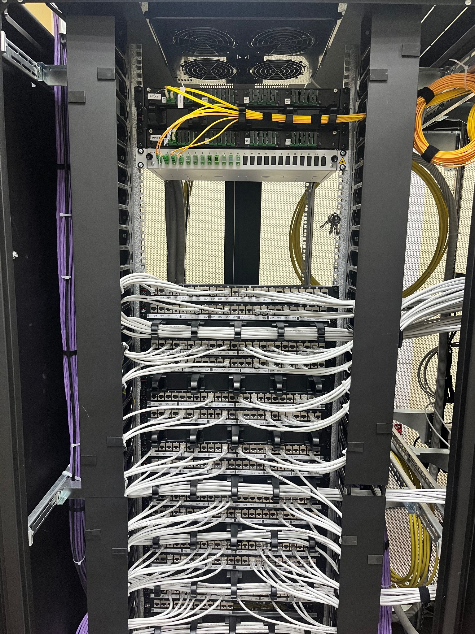 Uporządkowana szafa serwerowa z panelami krosowniczymi i estetycznie ułożonymi kablami w kolorach białym, żółtym i fioletowym. Widoczne wentylatory i klucze.