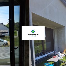 Pucujemyto - Czyszczenie okna z zewnątrz widoczne z wewnątrz, z logo firmy sprzątającej PucujemyTo nałożonym na zdjęcie, budynek w tle.