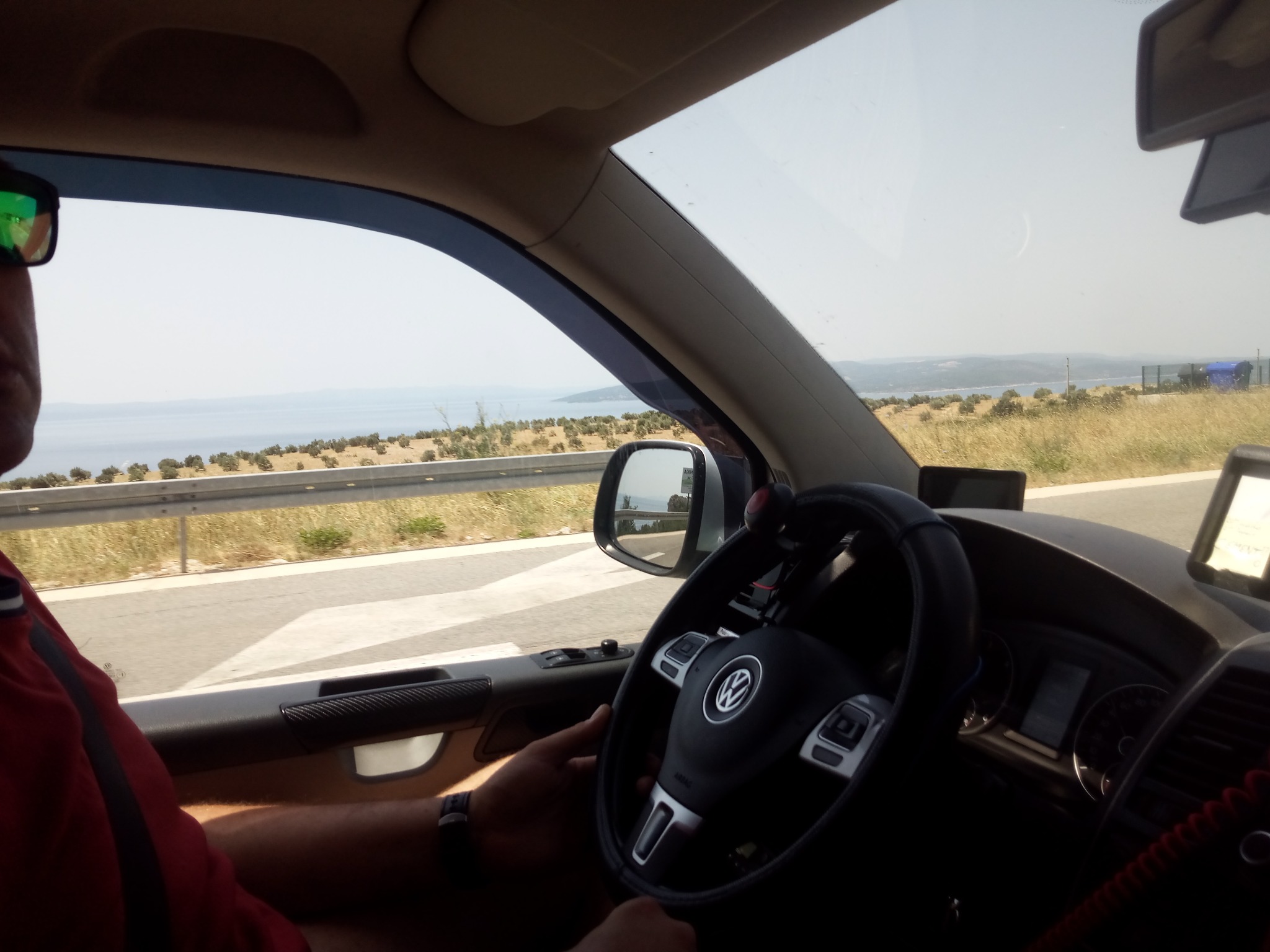 Wnętrze samochodu Volkswagen z widokiem na krajobraz nadmorski podczas jazdy w słoneczny dzień.