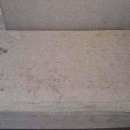 Monika Winiarska - Beżowa tapicerka kanapy z widocznymi, ciemnymi plamami i okrągłymi zaciekami, wymagająca odświeżenia.
