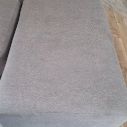 Monika Winiarska - Fragment szarej kanapy z widoczną fakturą materiału, sfotografowany w Kielcach, z drewnianą podłogą w tle.