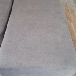 Fragment szarej kanapy z widoczną fakturą materiału, sfotografowany w Kielcach, z drewnianą podłogą w tle.