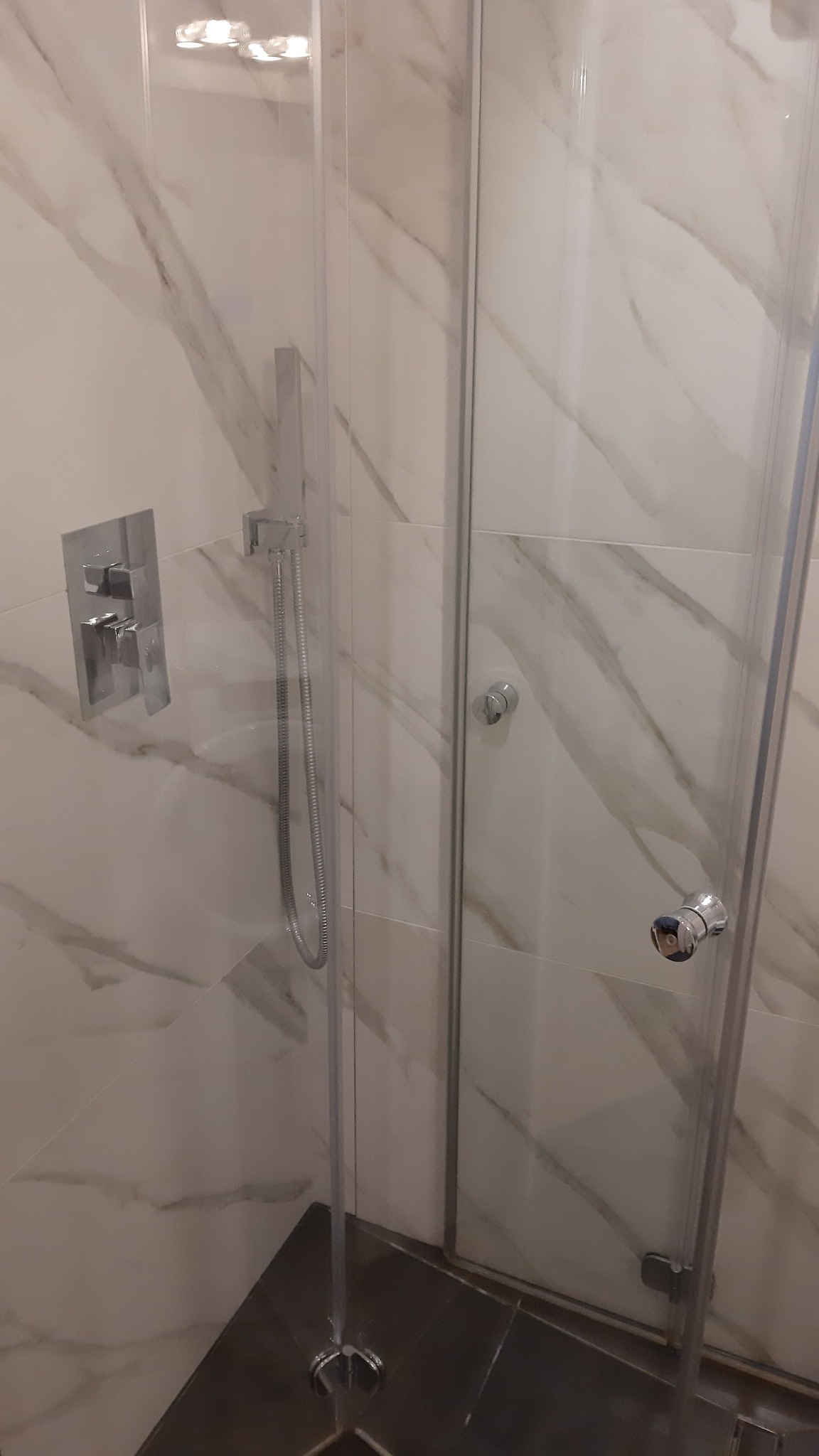 Nowoczesna kabina prysznicowa z marmurowymi płytkami, chromowaną armaturą i szklanymi drzwiami, widok z wnętrza kabiny.