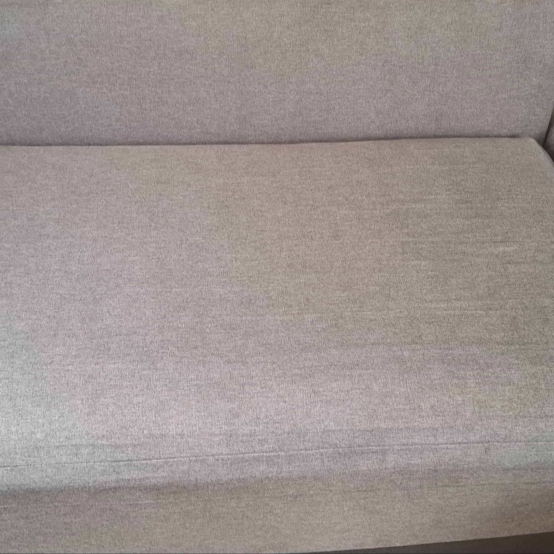 Szczegółowe ujęcie jasnoszarej, teksturowanej tapicerki kanapy z widocznym szwem.