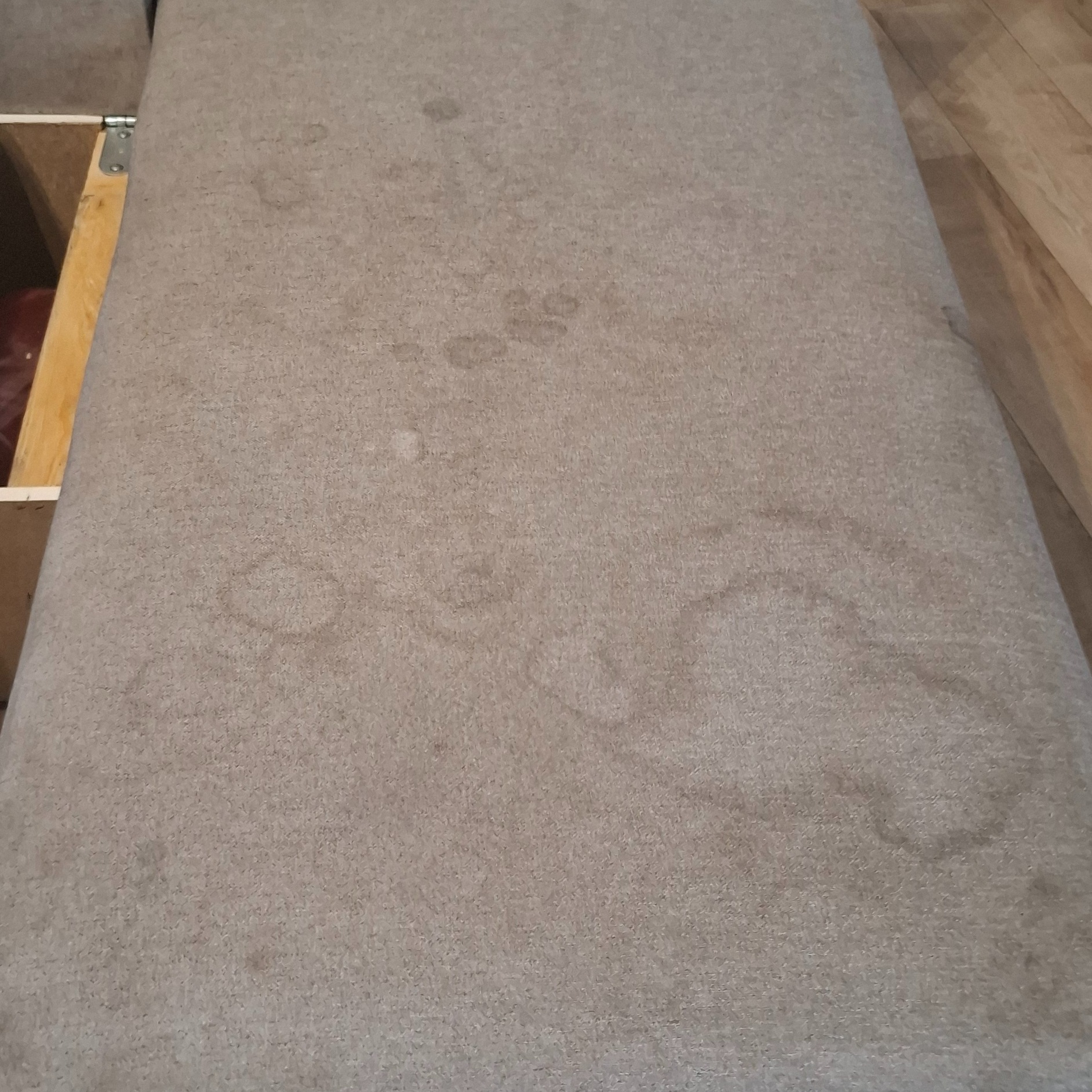 Beżowa tapicerka kanapy z widocznymi, okrągłymi plamami po cieczy, ukazująca potrzebę czyszczenia. Widoczna drewniana konstrukcja kanapy.