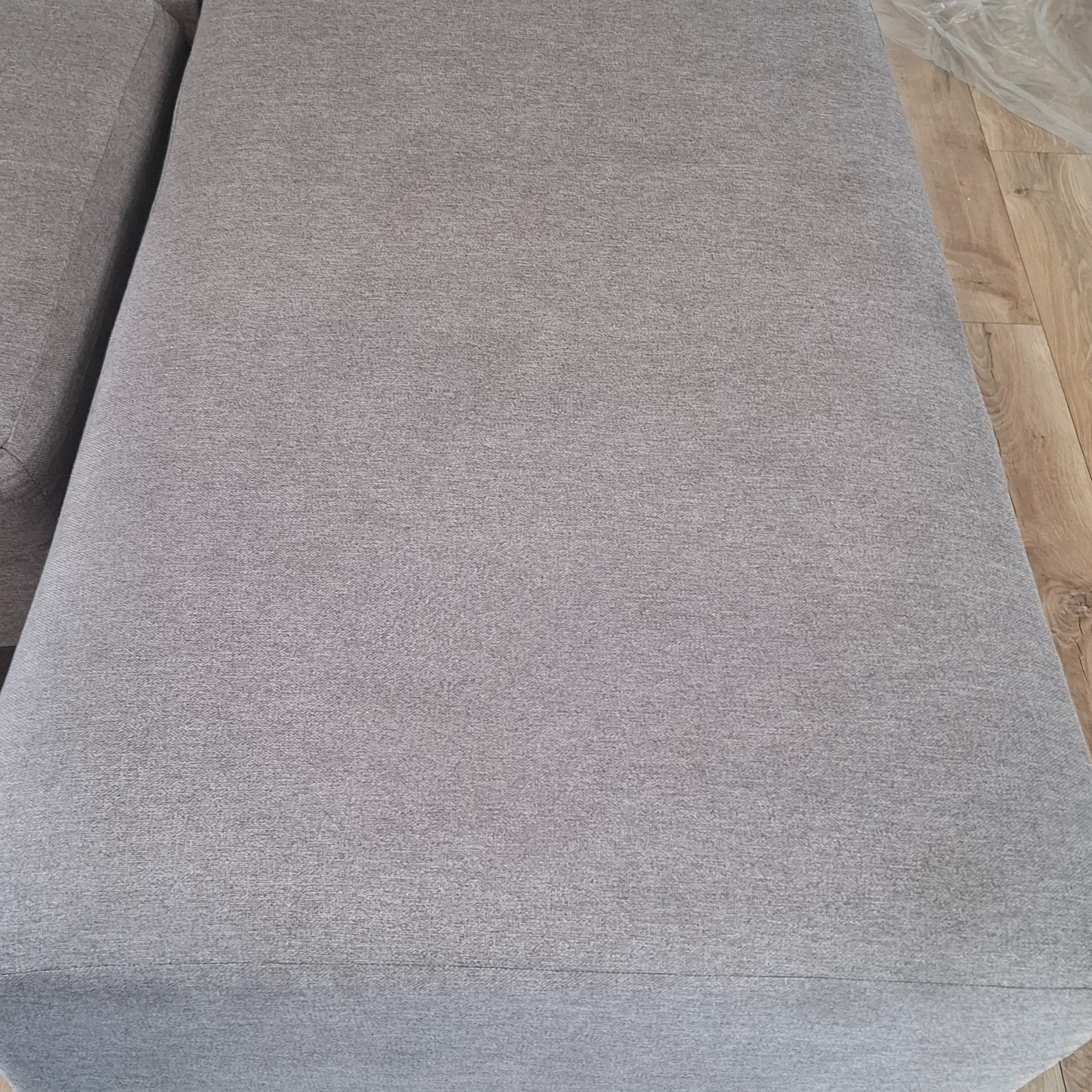 Fragment szarej kanapy z widoczną fakturą materiału, sfotografowany w Kielcach, z drewnianą podłogą w tle.