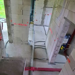 Paweł Gutowski GPJ Energia - Wnętrze budynku w trakcie budowy z widocznymi instalacjami elektrycznymi w rurkach ochronnych oraz przewodami poprowadzonymi po ścianach z betonu komórkowego, na których widoczne są oznaczenia...