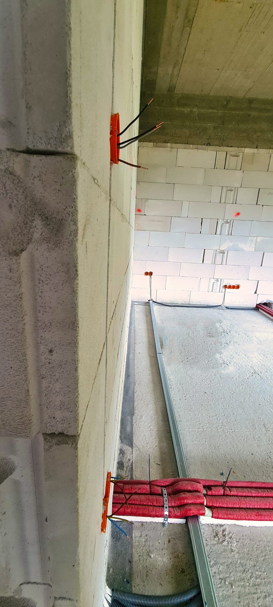 Wewnętrzna instalacja elektryczna w surowym stanie, widoczne puszki instalacyjne z wystającymi przewodami w ścianie z bloczków betonowych oraz rury w izolacji termicznej mocowane do metalowej...