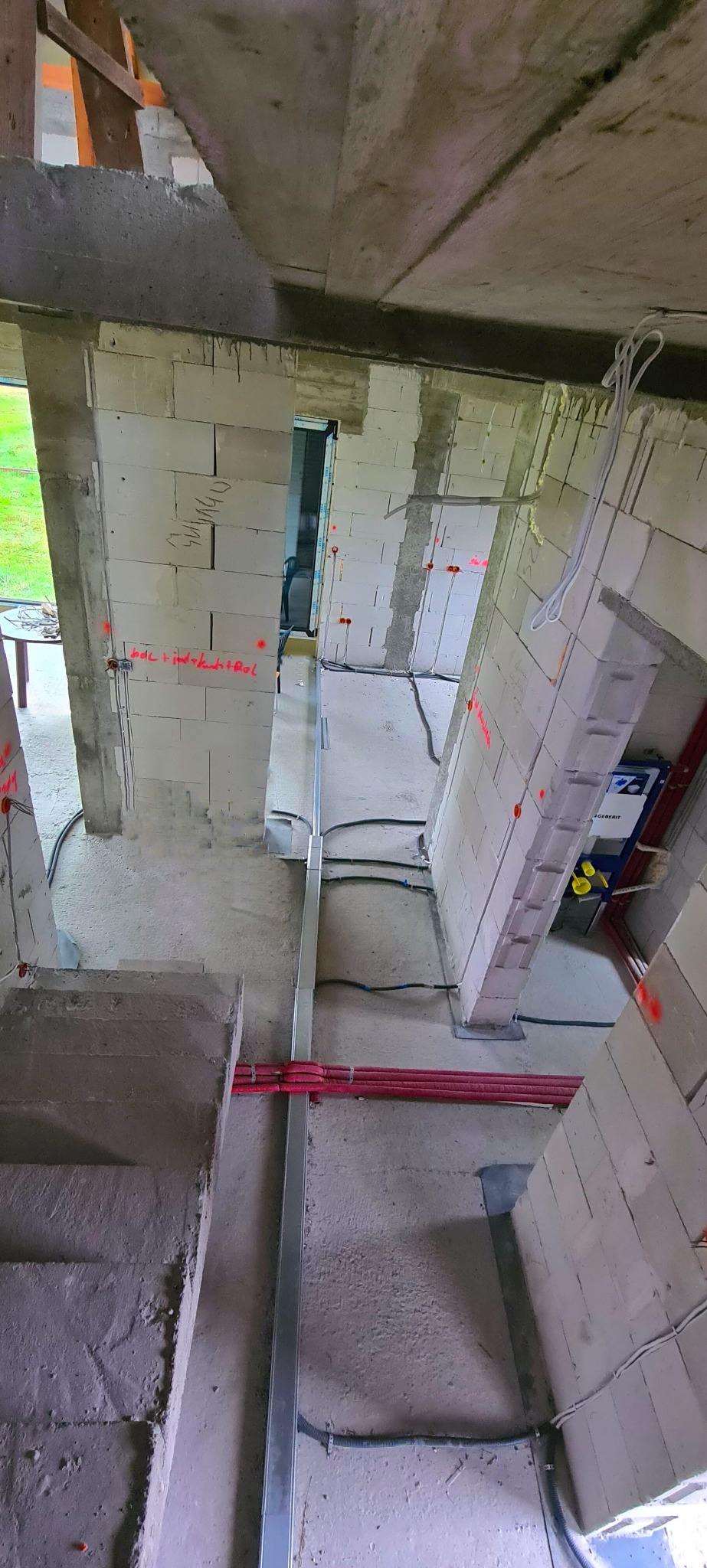 Wnętrze budynku w trakcie budowy z widocznymi instalacjami elektrycznymi w rurkach ochronnych oraz przewodami poprowadzonymi po ścianach z betonu komórkowego, na których widoczne są oznaczenia...