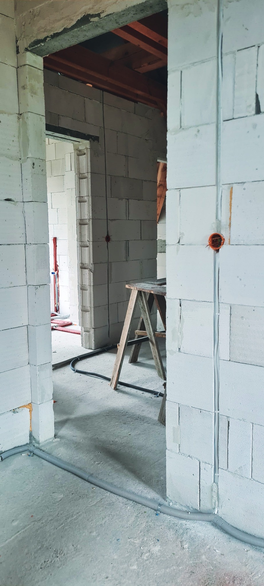 Wnętrze w trakcie budowy z widocznymi przewodami elektrycznymi w ścianach z betonu komórkowego oraz peszlem na podłodze i skrzynką elektryczną w ścianie.