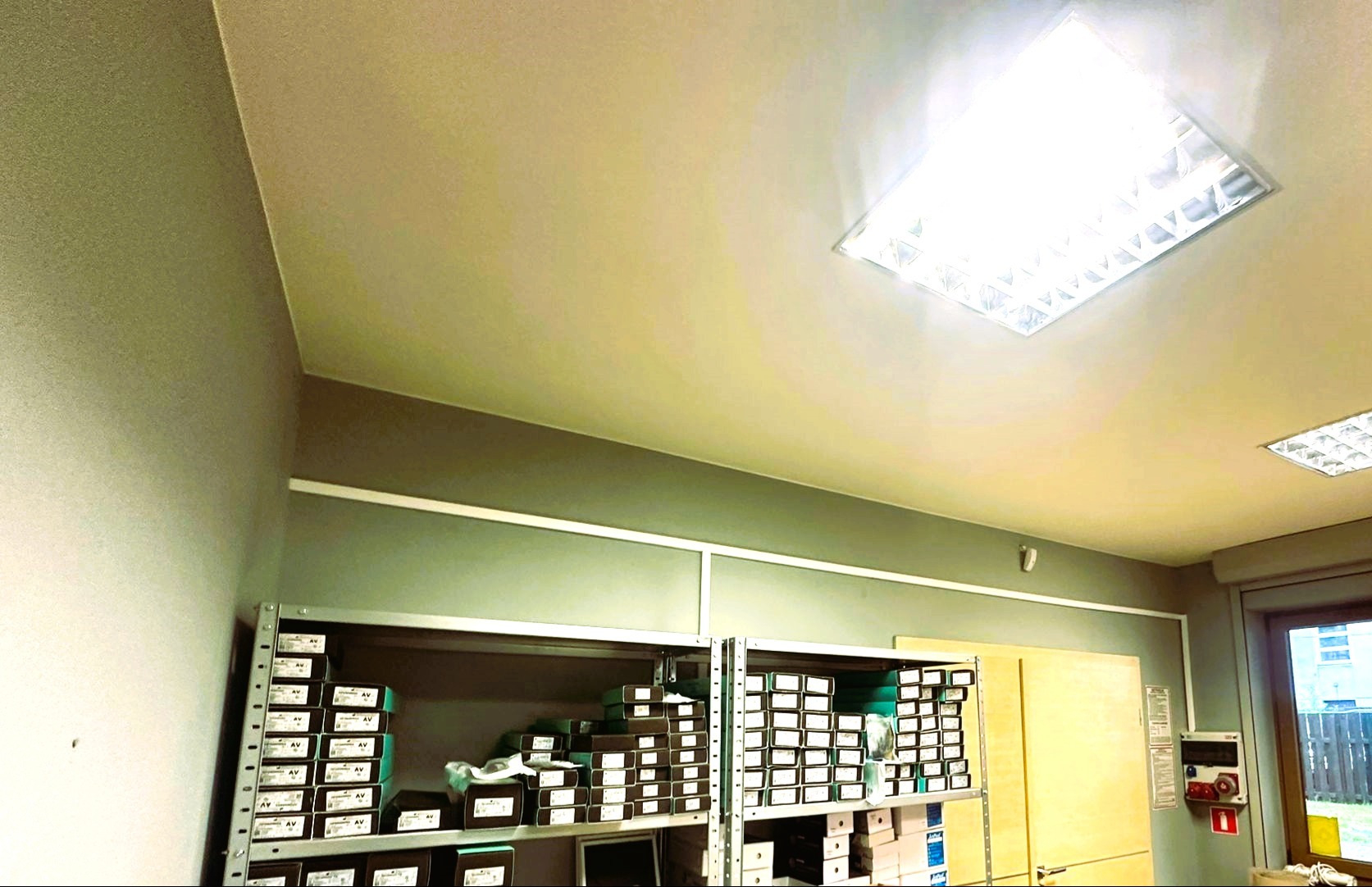 Magazyn z półkami wypełnionymi pudełkami z komponentami elektrycznymi pod oświetleniem rastrowym.