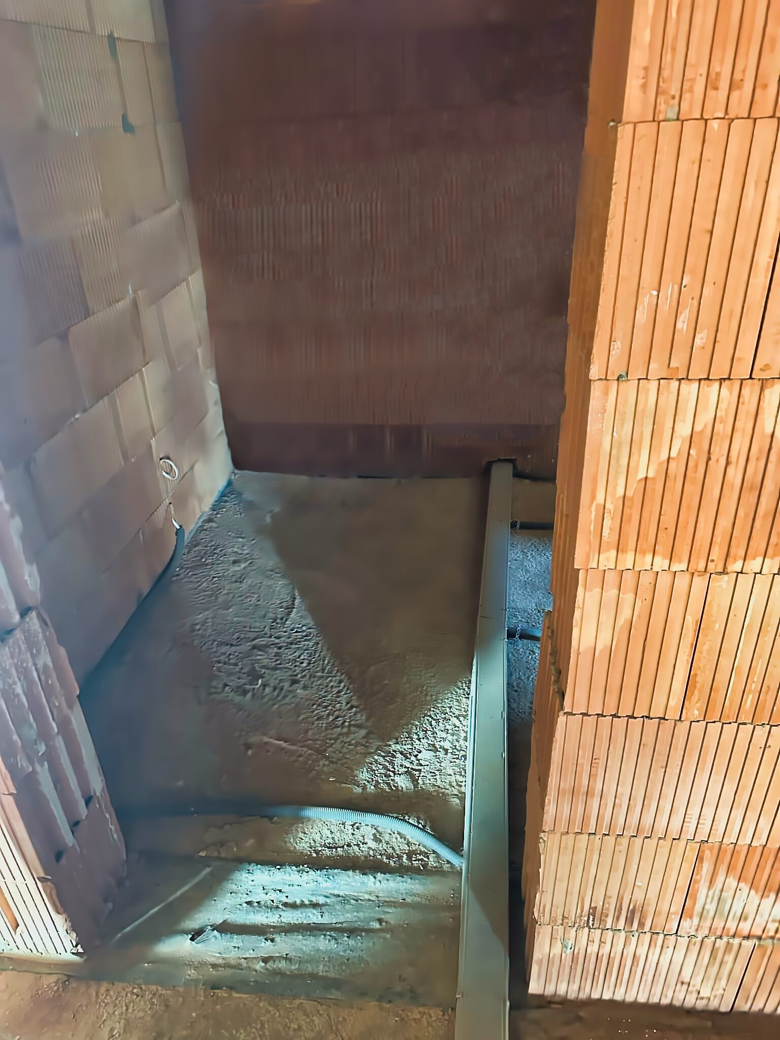 Wewnętrzna ściana z czerwonej cegły z widoczną rurą karbowaną w podłodze podczas wylewki betonowej.