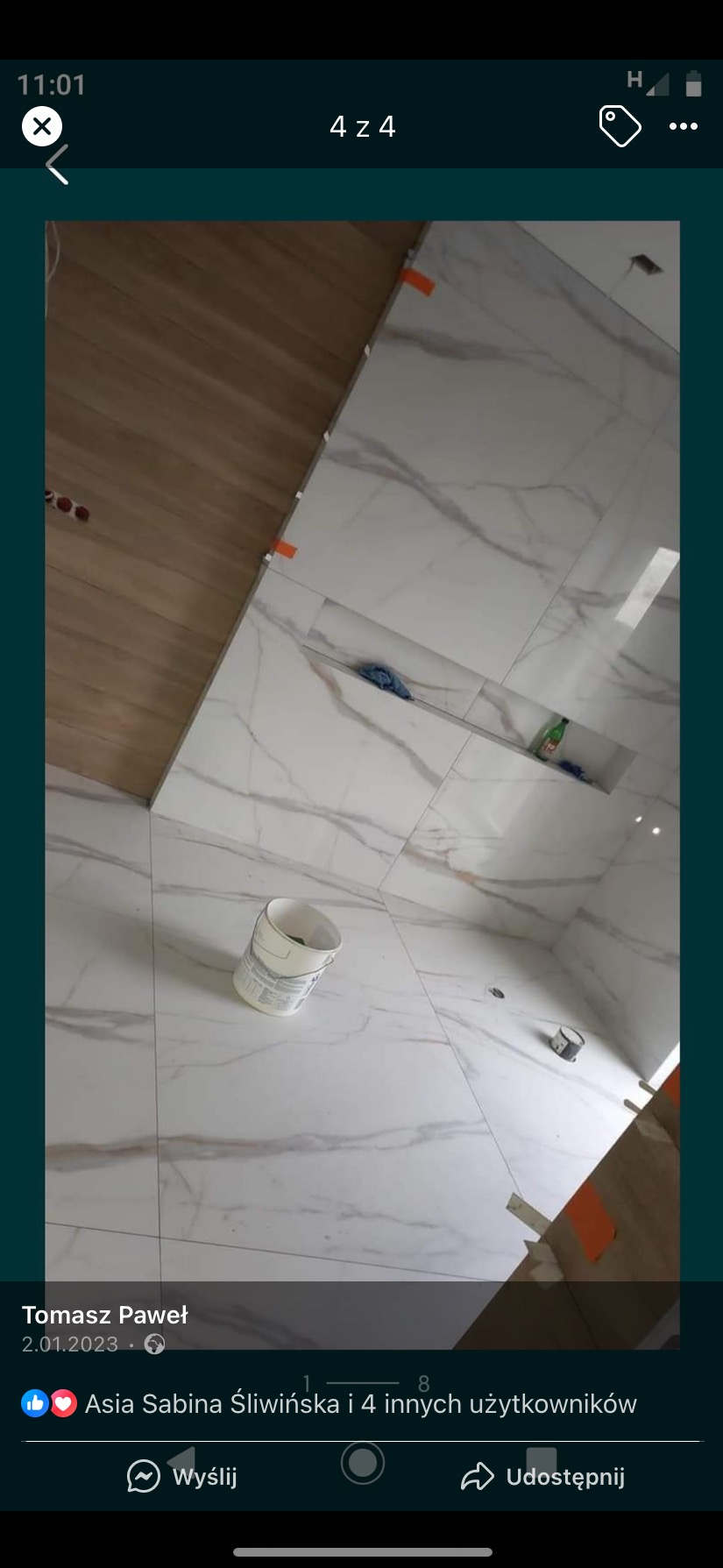 Świeżo ułożone, marmurowe płytki w łazience z wnękami, widoczne narzędzia i wiadro, częściowo wykończona podłoga z paneli.