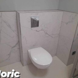 Moric - Zawieszona toaleta z płytkami imitującymi marmur i chromowanym przyciskiem spłukującym, wykończona listwami w kolorze aluminium.