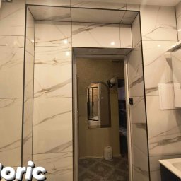 Moric - Wykończona łazienka w Pile z białymi płytkami imitującymi marmur, czarnymi fugami i grzejnikiem drabinkowym po lewej stronie.