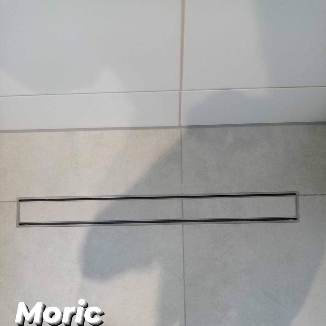 Ułożona podłoga z jasnych, kwadratowych płytek ceramicznych z zamontowanym liniowym odpływem podłogowym z czarną szczeliną.