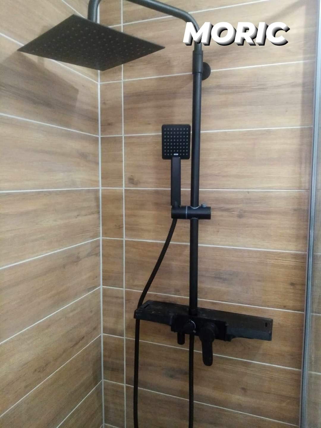 Czarny zestaw natryskowy z deszczownicą i baterią termostatyczną zamontowany na ścianie wyłożonej płytkami imitującymi drewno.