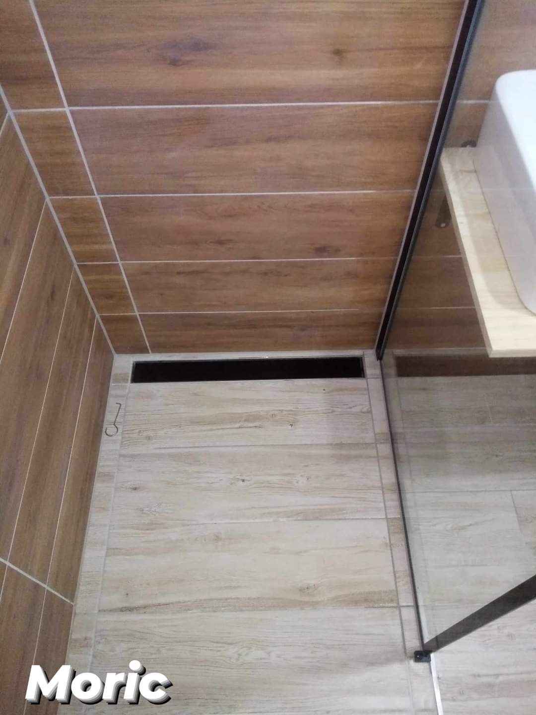 Nowoczesny odpływ liniowy w kabinie prysznicowej wyłożonej płytkami imitującymi drewno w łazience w Pile.