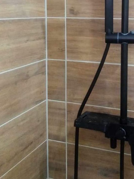 Fragment łazienki z brązowymi płytkami imitującymi drewno i czarną armaturą prysznicową.