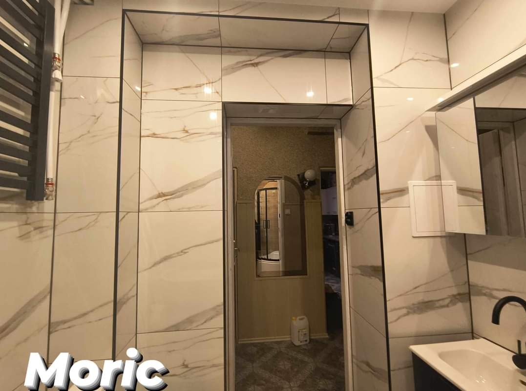 Wykończona łazienka w Pile z białymi płytkami imitującymi marmur, czarnymi fugami i grzejnikiem drabinkowym po lewej stronie.