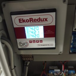 Pan ElektRyK - Panel sterowania EkoRedux w szarej obudowie, wyświetlający wartości 420 i 421, z widocznymi przewodami i elementami instalacji elektrycznej w tle.