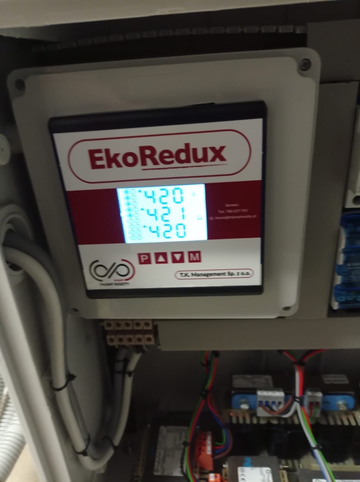Panel sterowania EkoRedux w szarej obudowie, wyświetlający wartości 420 i 421, z widocznymi przewodami i elementami instalacji elektrycznej w tle.