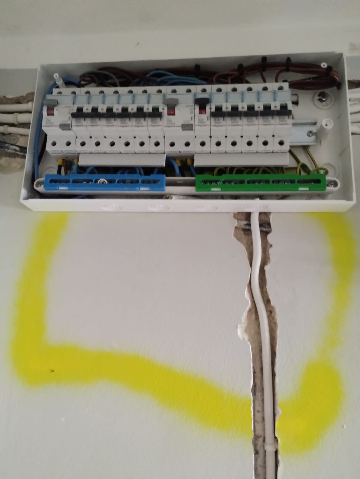 Otwarta skrzynka bezpiecznikowa z zainstalowanymi bezpiecznikami i przewodami, widoczne ślady po wcześniejszej instalacji na ścianie z żółtymi oznaczeniami.