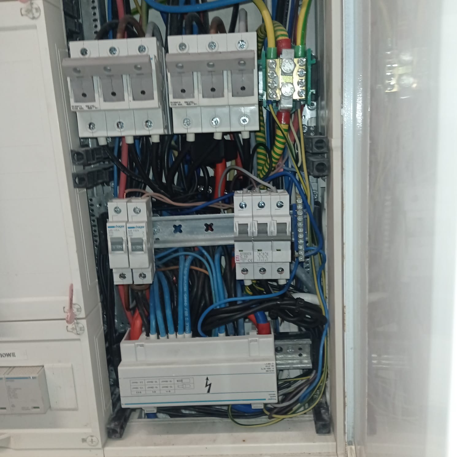 Otwarta skrzynka elektryczna z bezpiecznikami, przewodami w różnych kolorach i złączkami, widoczne elementy montażowe i opis na listwie.