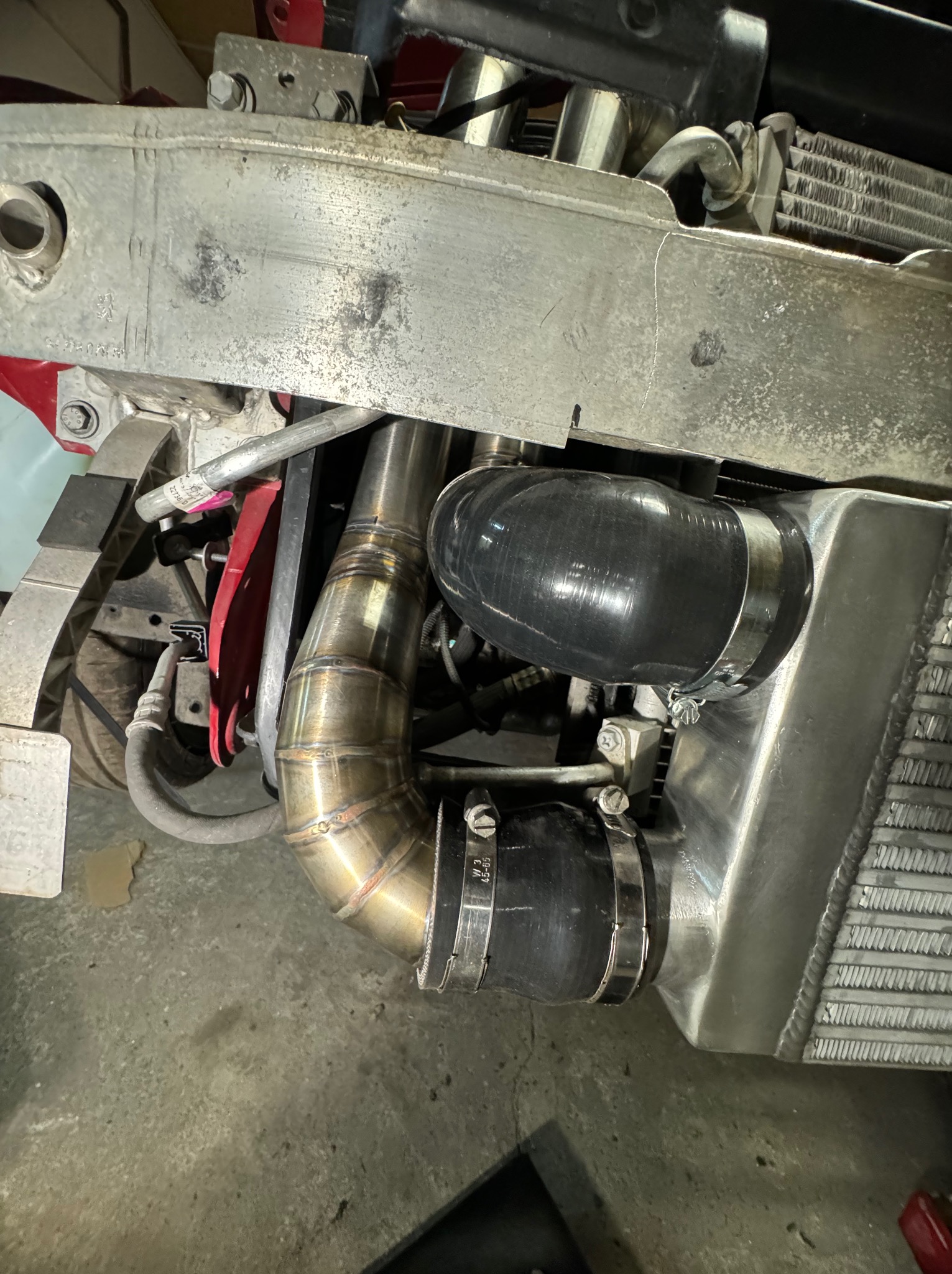 Zespawane rury dolotowe intercoolera w samochodzie, widoczne spawy i metalowe obejmy.