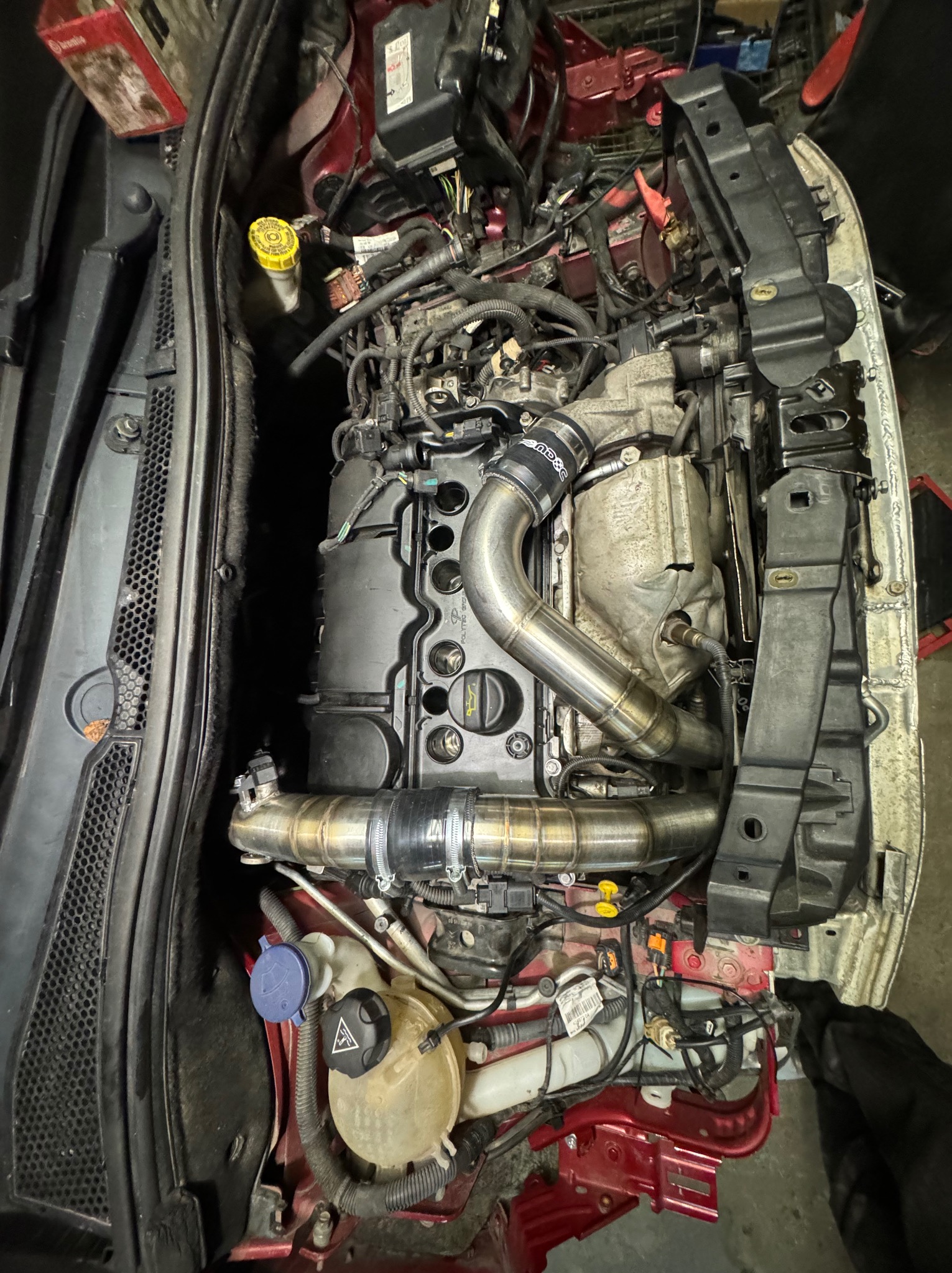 Widok z góry na silnik samochodowy z widocznymi elementami układu dolotowego powietrza wykonanymi z polerowanej stali nierdzewnej, widoczne płyny eksploatacyjne, elementy karoserii w kolorze...