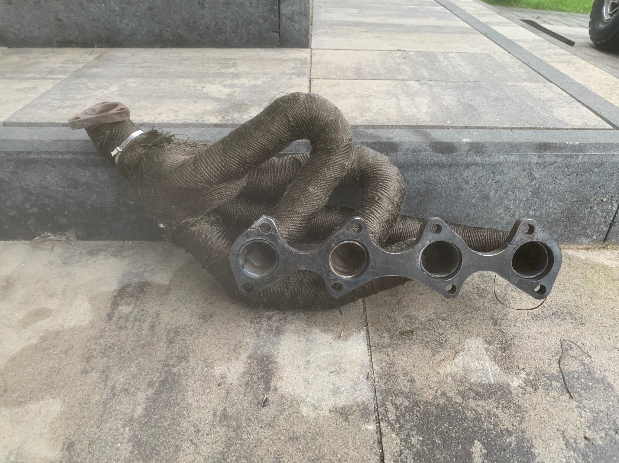 Kolektor wydechowy owinięty termoizolacyjną taśmą leżący na betonowej powierzchni.