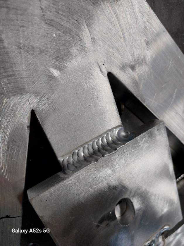 Szlifowana powierzchnia metalu z widocznym spoiną wykonaną metodą TIG, spaw łączący elementy o geometrycznych kształtach.