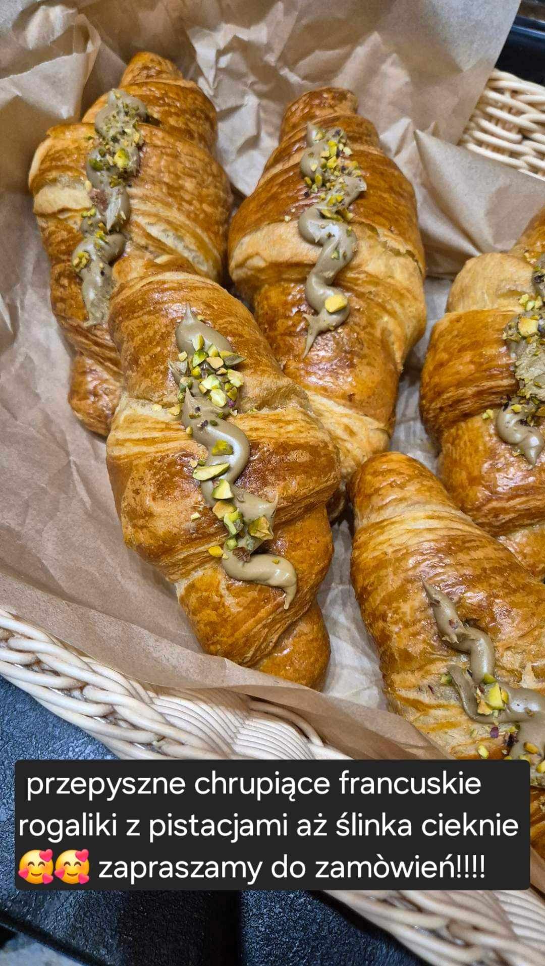 Świeżo upieczone, złociste croissanty z kremem pistacjowym i posypką z posiekanych pistacji, ułożone w wiklinowym koszyku wyłożonym papierem pergaminowym.