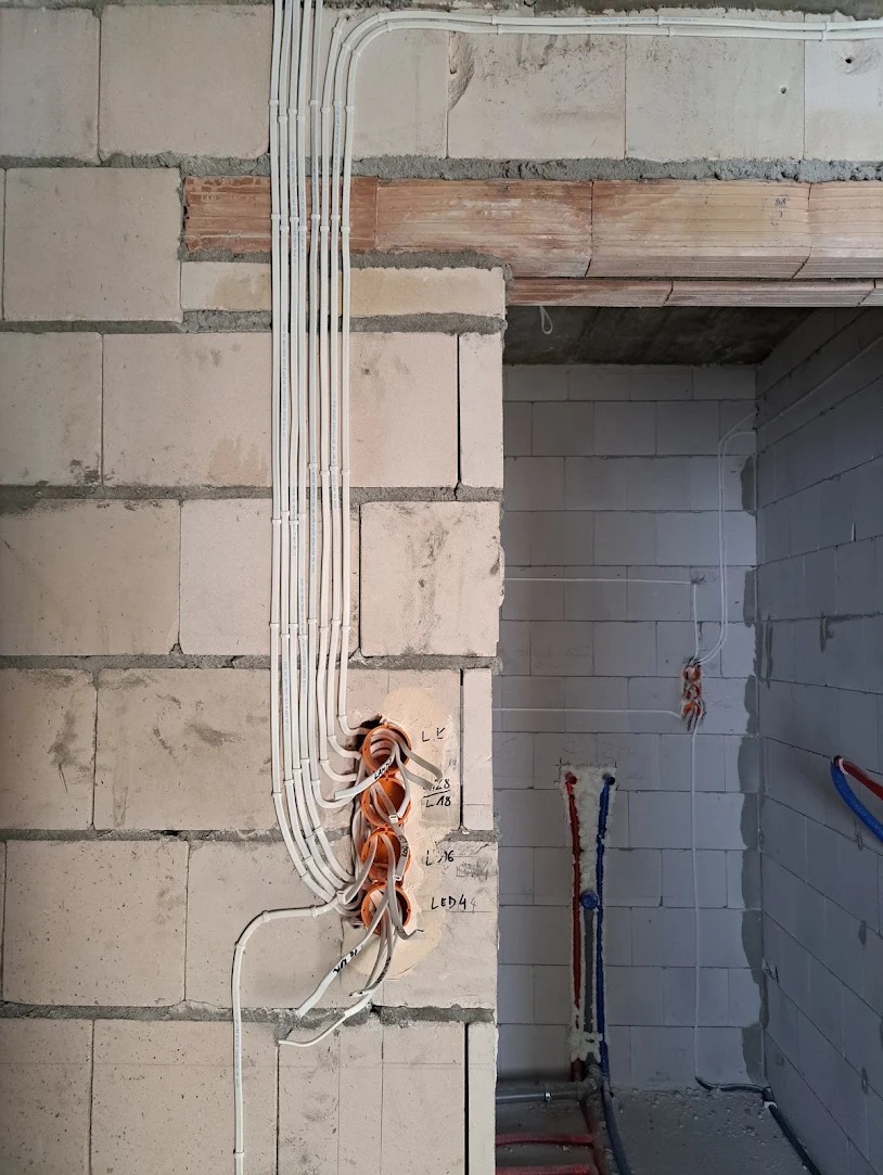 Instalacja elektryczna w surowym wnętrzu: pionowe rury kablowe prowadzone wzdłuż ściany z betonu komórkowego, okrągłe puszki instalacyjne z widocznymi przewodami, instalacja wodna w pianie...