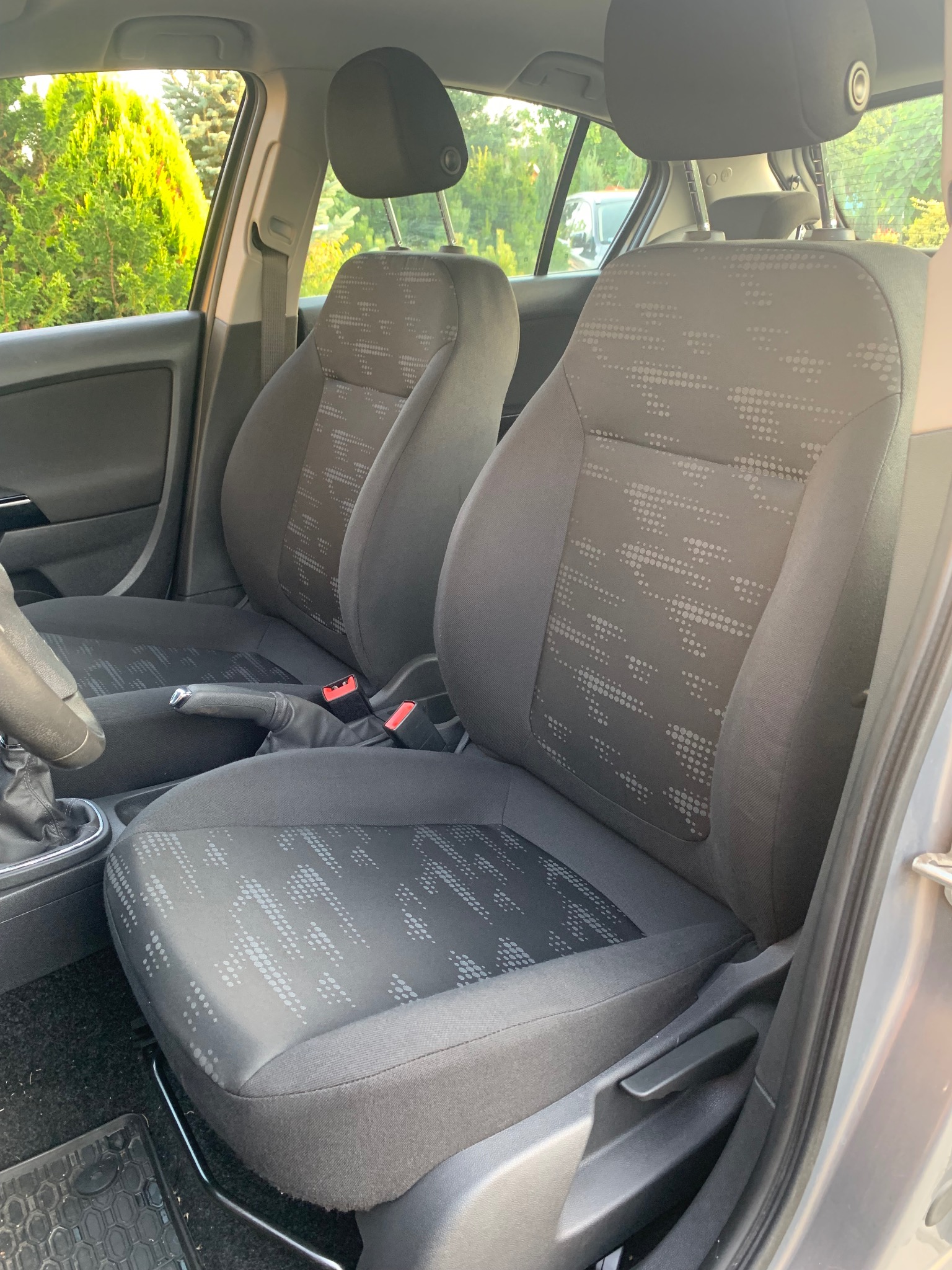 Wnętrze samochodu z widocznymi czystymi, szarymi fotelami z delikatnym wzorem w kropki, uchwyconymi w naturalnym oświetleniu dziennym.