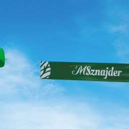 Arabeska Art & Brand Design - Zielony samolot ciągnie za sobą baner z napisem 'MSznajder' na tle błękitnego nieba z delikatnymi chmurami.