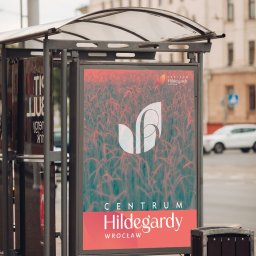 Arabeska Art & Brand Design - Billboard reklamowy z logo Centrum Hildegardy we Wrocławiu, umieszczony na przystanku autobusowym, z tłem przedstawiającym abstrakcyjny wzór przypominający pole pszenicy.