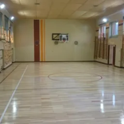 Sala gimnastyczna z parkietem w jodełkę, drabinkami i ścianką wspinaczkową. Parkiet po renowacji, z widocznymi liniami boiska.